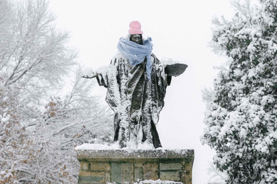A statue of Jesus on campus wrapped in a scarf and hat to keep Him warm in the snow.