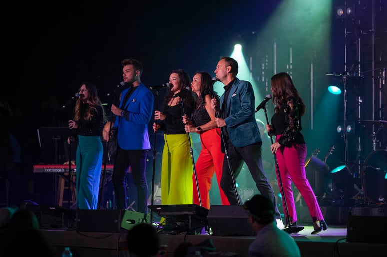 A group of performers singing on stage dressed in colorful outfits