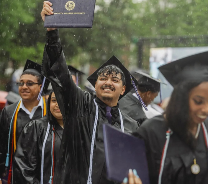 A recent Trevecca graduate holds up his diploma and smiles triumphantly in the rain.